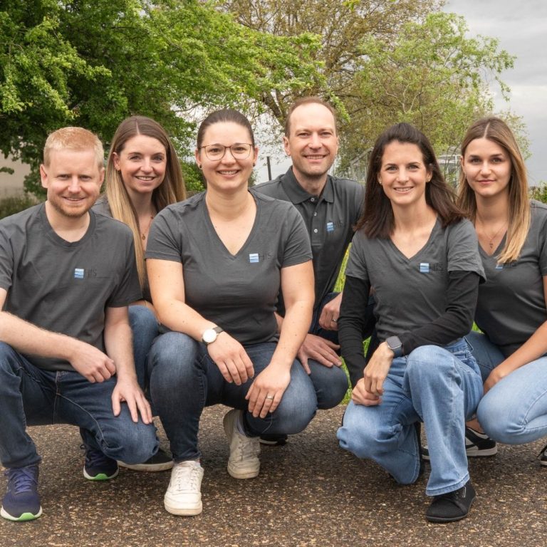 6 Teammitglieder sind abgebildet. Das Bild wurde in der Natur gemacht, im Hintergrund erkennt man Bäume.